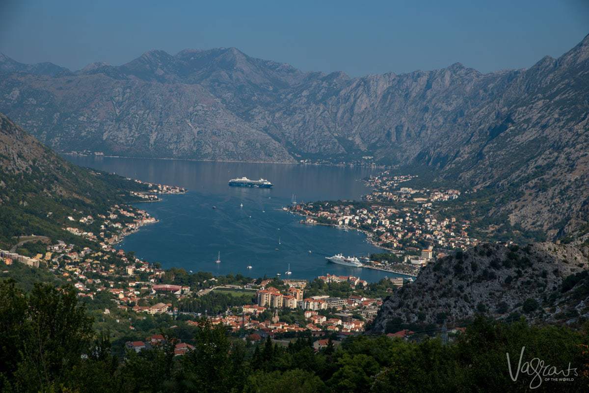 Looking down over the Bay of Kotor surrounded by magnificent mountains. A cruise ship is in the middle of the bay and villages dot the shoreline. 
