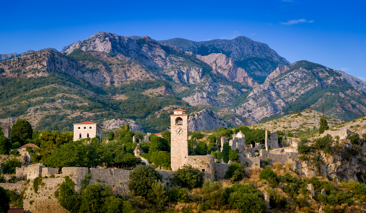 The clock tower and ruins of the ancient town of Stari bar in Montenegro with mountains in the distance and blue sky. 
